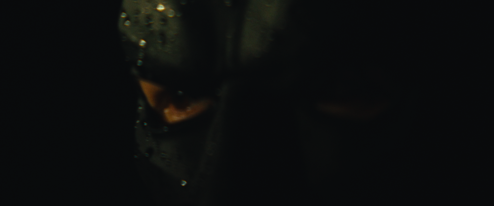 Close-up of a dark surface with water droplets and a partially visible orange and black object, possibly a flower or a fruit.