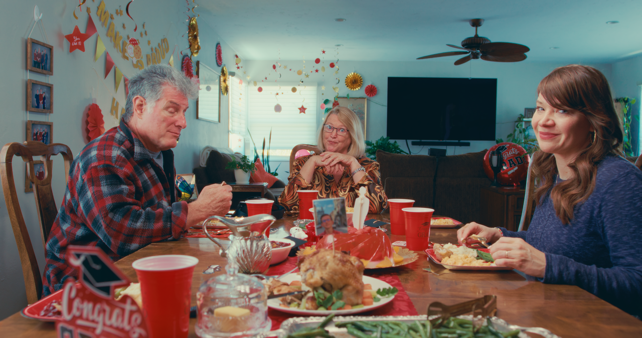 Family gathered around a table celebrating a graduation, with food and decorations in a decorated living room.