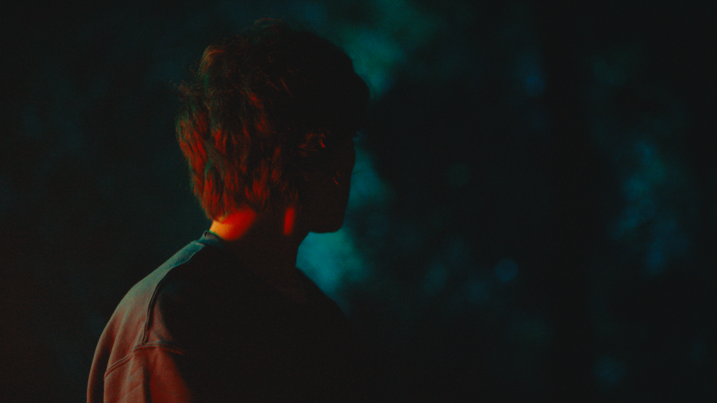 Silhouette of a person with short, messy hair, facing sideways with colorful lighting in dark environment.