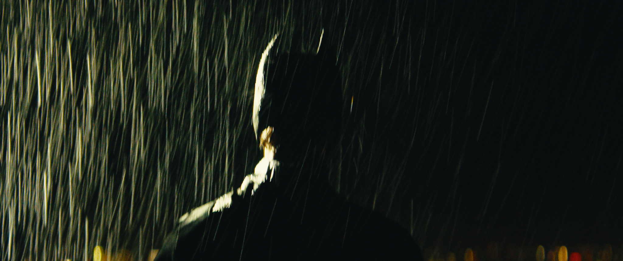 A person walking on a dark, rainy street at night, holding an umbrella.