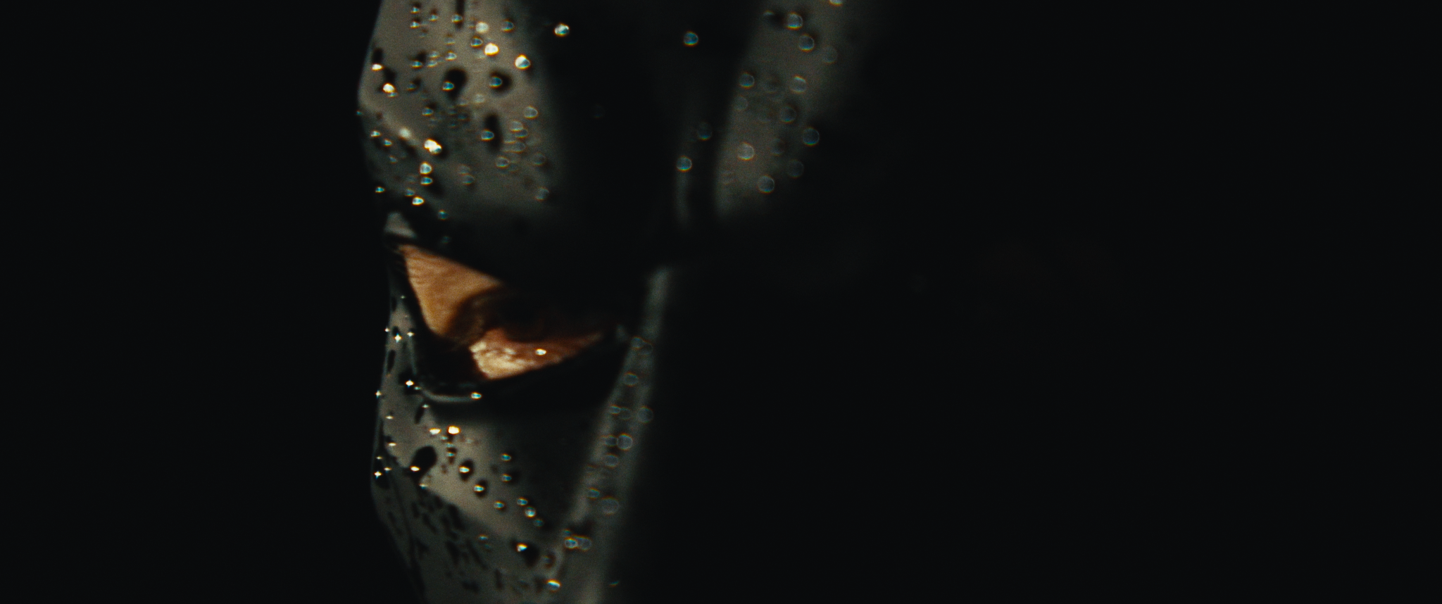 Close-up of a metallic object with water droplets on it, partially in shadow, with a dark background.