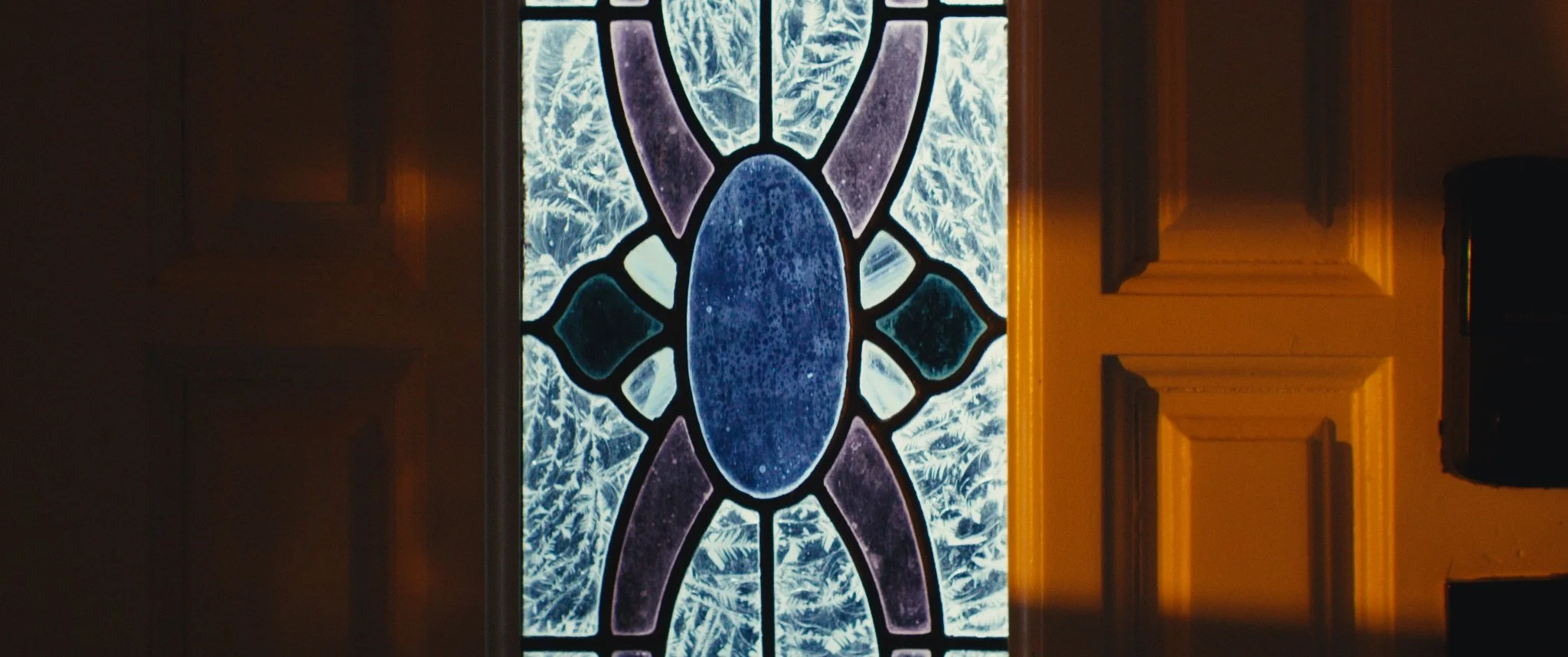 Decorative stained glass window with a design resembling a turtle, featuring various shades of blue and purple, surrounded by ornate wood paneling.