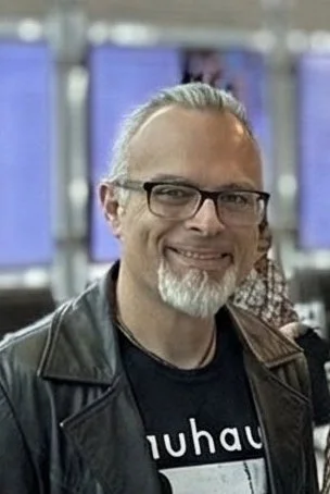 Smile of a man with glasses and a beard at an indoor event.