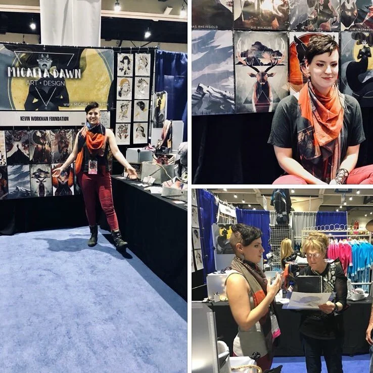 A woman stands at an art and design booth with artwork displayed behind her, smiling at the camera. Another woman and a man are engaged in conversation at a different booth, looking at a tablet and holding papers. The booths feature various art pieces, including animal and nature themes, with banners displaying the artist's name and works.