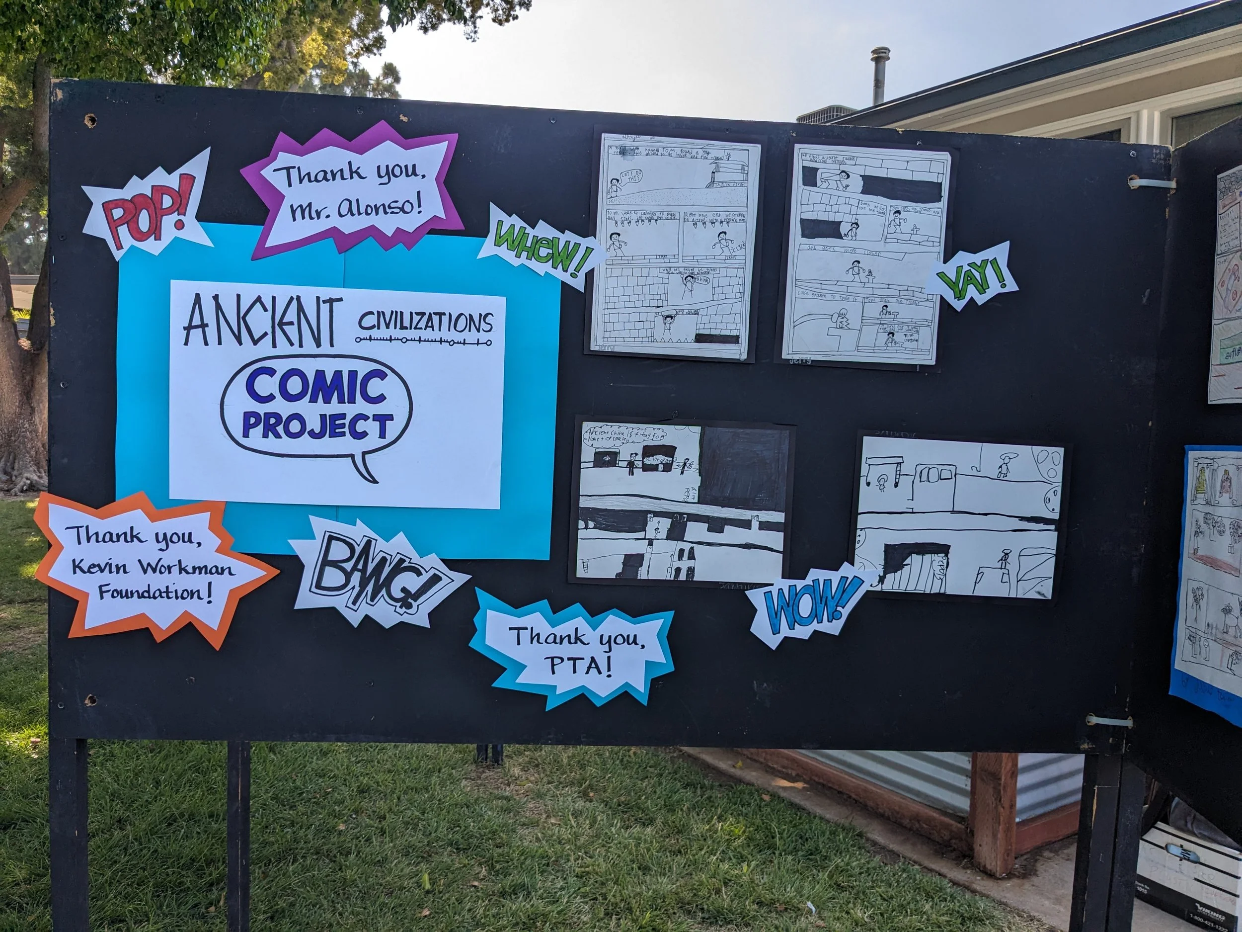 A display board with comic project drawings and signs expressing gratitude and excitement, including phrases like 'Thank you, Mr. Alonso!', 'WOW!', 'YAY!', and 'Thank you, Kevin Workman Foundation!'