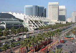 Downtown area with modern skyscrapers, a train station with a curved roof, and palm trees along the street