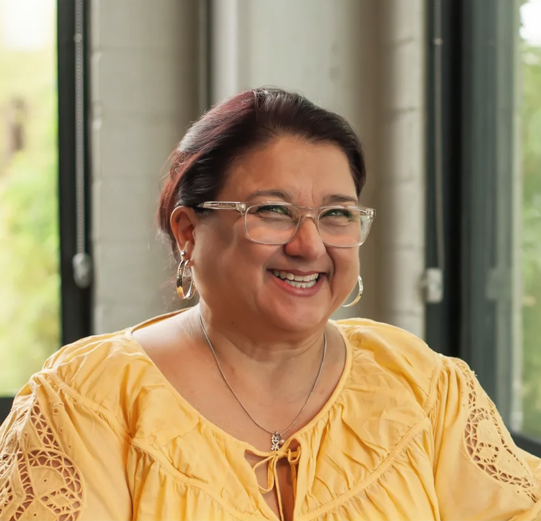 Portrait of a woman with shoulder-length dark hair, smiling, wearing a burgundy patterned top and a delicate necklace.