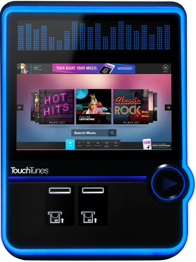 A TouchTunes Jukebox with a colorful screen displaying a music playlist interface, labeled 'TouchTunes,' with buttons and a circular control pad on the front, surrounded by a blue glowing border.