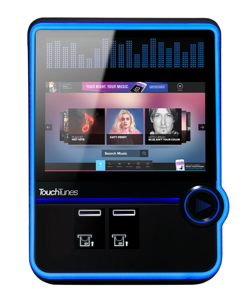 A neon-lit touchscreen TouchTunes jukebox displaying a music search interface with images of Katy Perry, Keith Urban, and a playlist titled 'Hot Hits.'