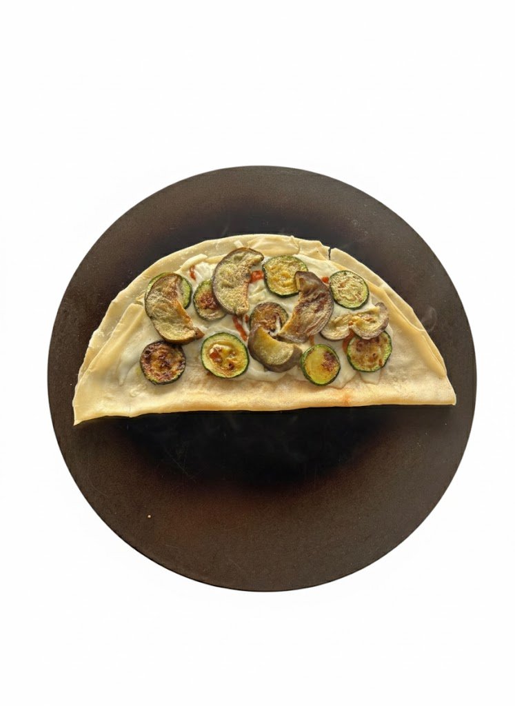 A slice of vegetable pizza topped with zucchini slices on a black plate