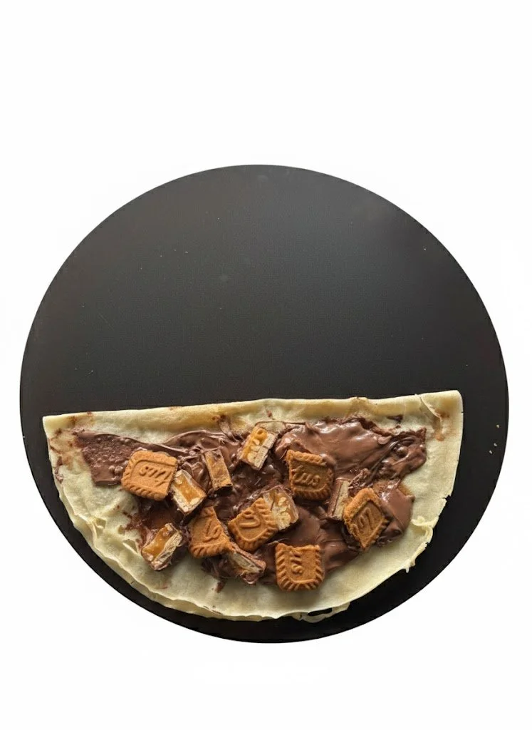A slice of dessert with chocolate, Kit Kat pieces, and white chocolate on a black circular plate.
