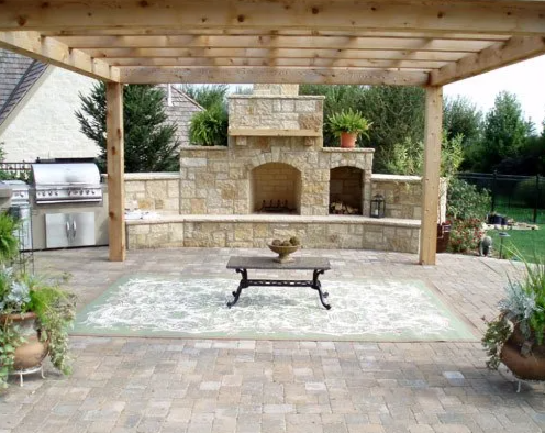 Outdoor patio with a stone fireplace, a wooden pergola overhead, and potted plants on the sides.
