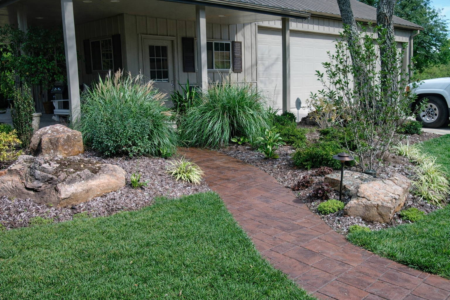 A well-maintained front yard with a brick pathway leading to a house, landscaped with various shrubs, rocks, and garden lights.