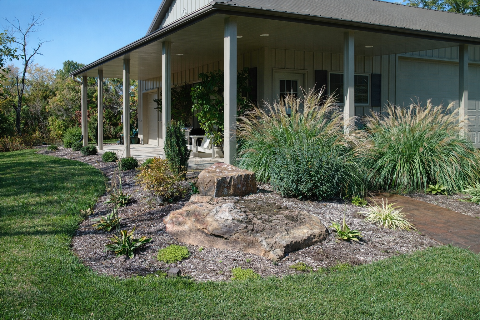 Front view of a house with a covered porch, surrounded by a landscaped garden with large rocks, bushes, ornamental grasses, and a brick pathway.