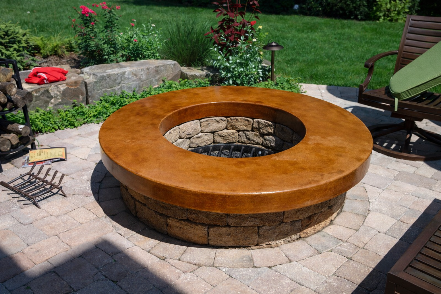 Round firepit with a stone base and a wooden top surrounded by outdoor chairs and plants on a paved patio.