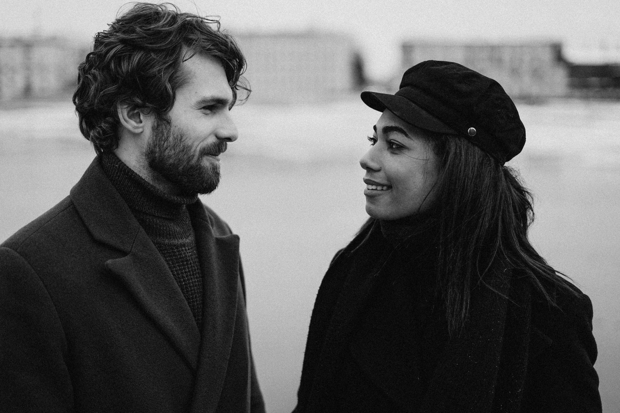 A man and woman standing outdoors, facing each other and smiling, in a black and white photo.