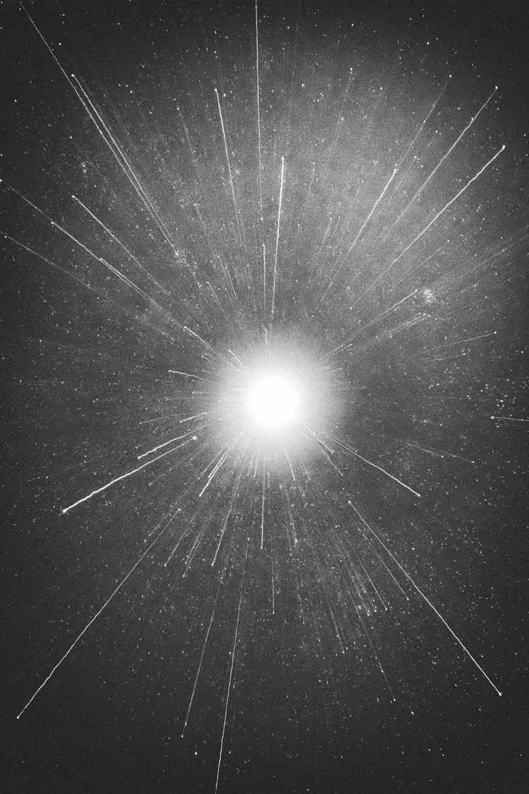 Bright explosion or burst of light in space with streaks radiating outward, against a background filled with stars.