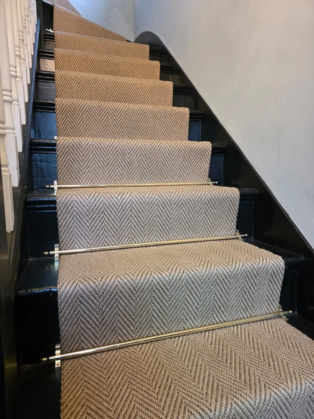 Carpeted stairs with beige and brown herringbone pattern, black risers, and metal rods across each step, leading up a staircase.