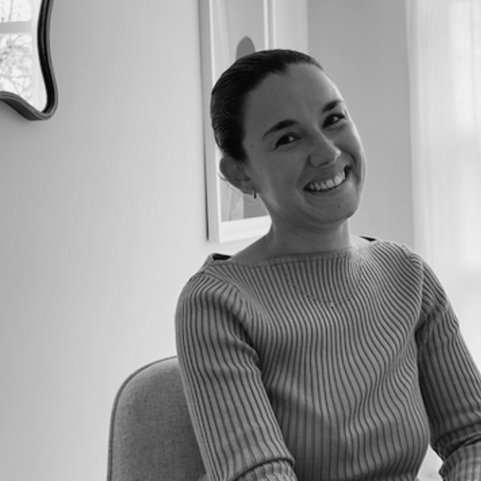 Smiling woman sitting in a chair in a room with framed pictures on the wall.