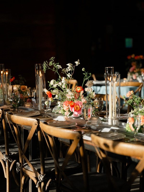 A dining table set for an event, decorated with a floral centerpiece, tall candles, glassware, and plates.