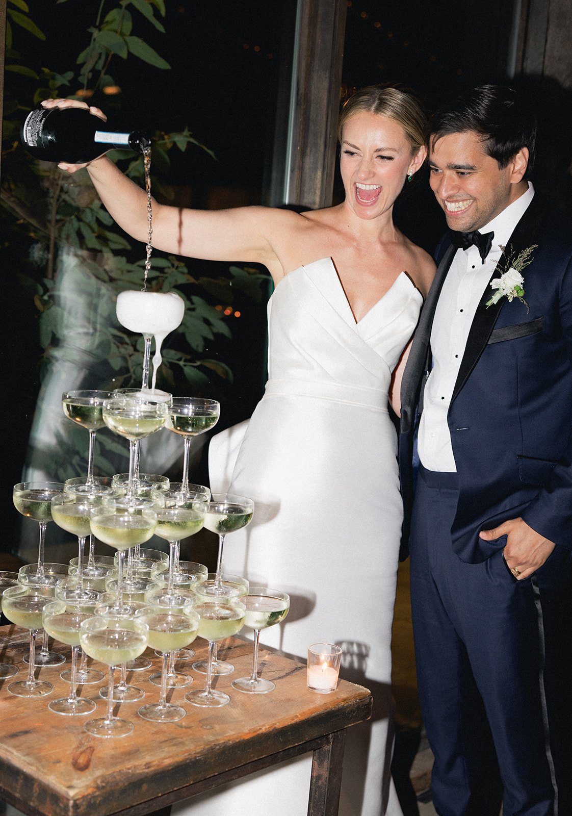 A bride and groom celebrating at their wedding, pouring and enjoying champagne from a champagne tower.