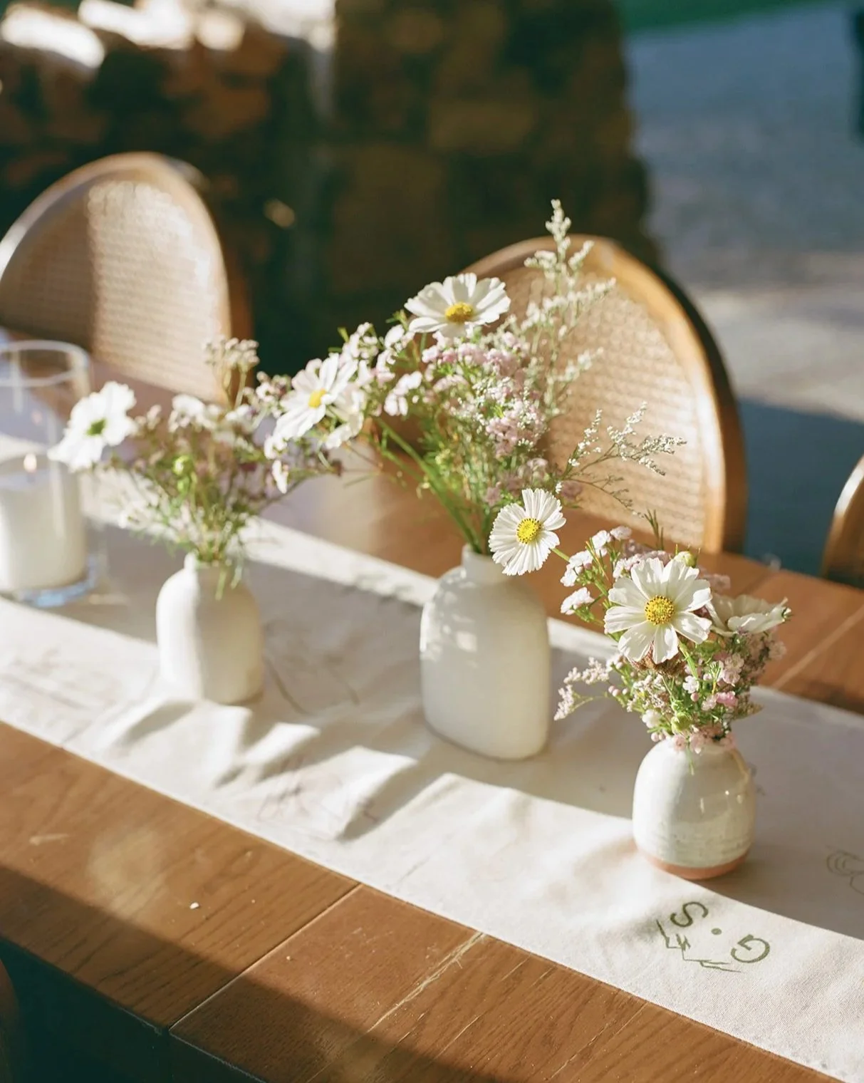 Table with three small white vases holding white and pink flowers, a glass candle, and a white table runner.
