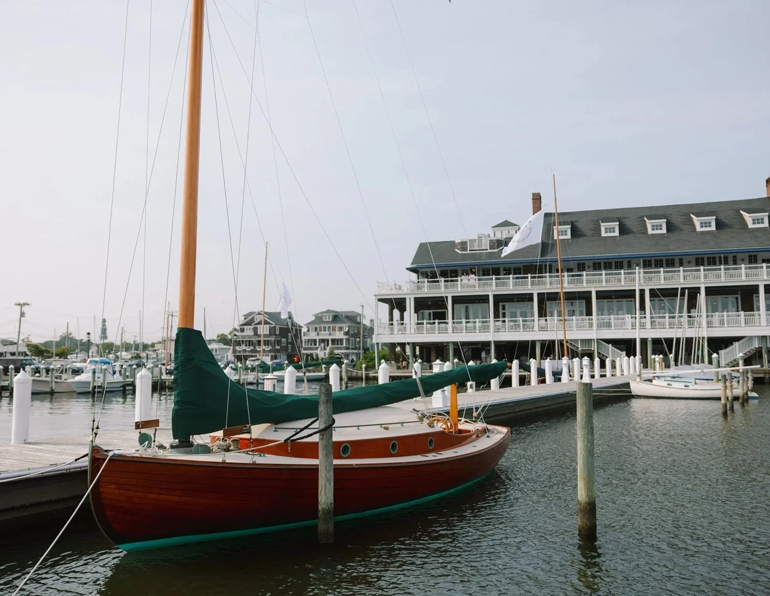 Sailboat docked at a marina with multi-story waterfront buildings in the background.