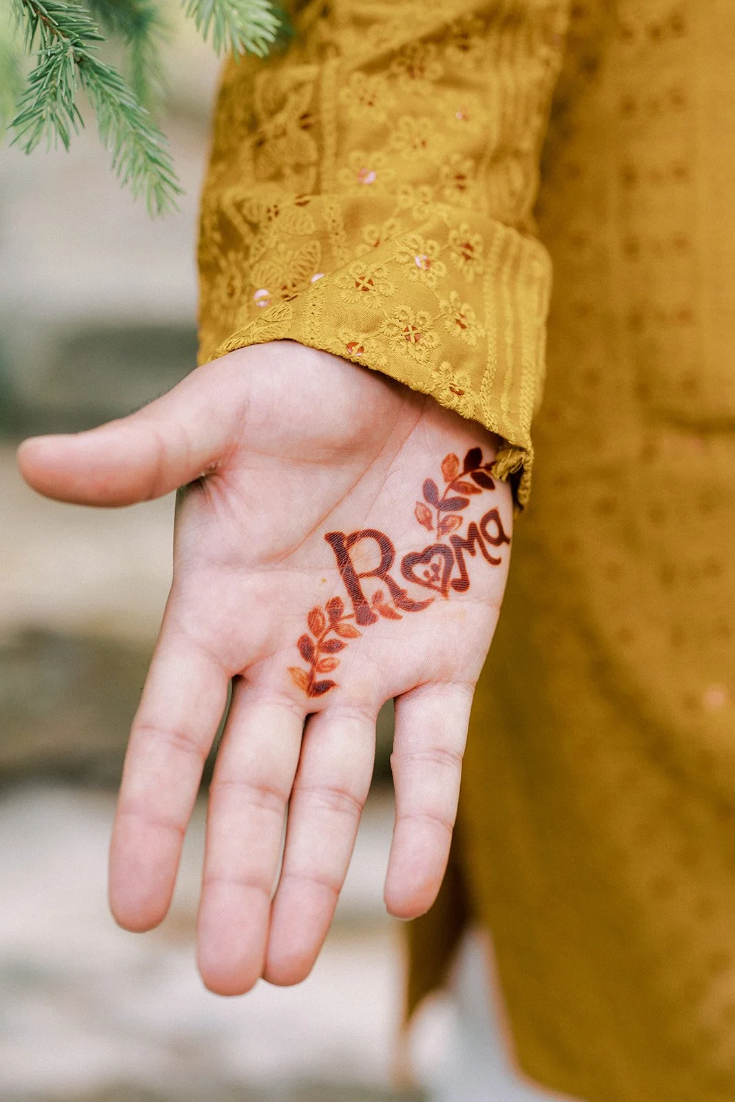 A person's hand with a temporary tattoo that reads 'LOVE' with a decorative leaf design. The person is wearing a yellow embroidered sleeve.