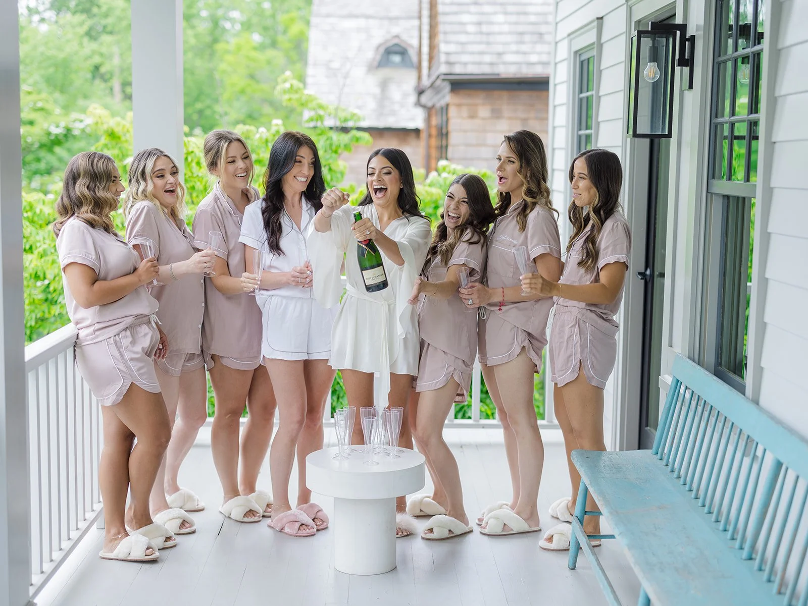 A group of women in pajamas celebrating on a porch with champagne bottles.
