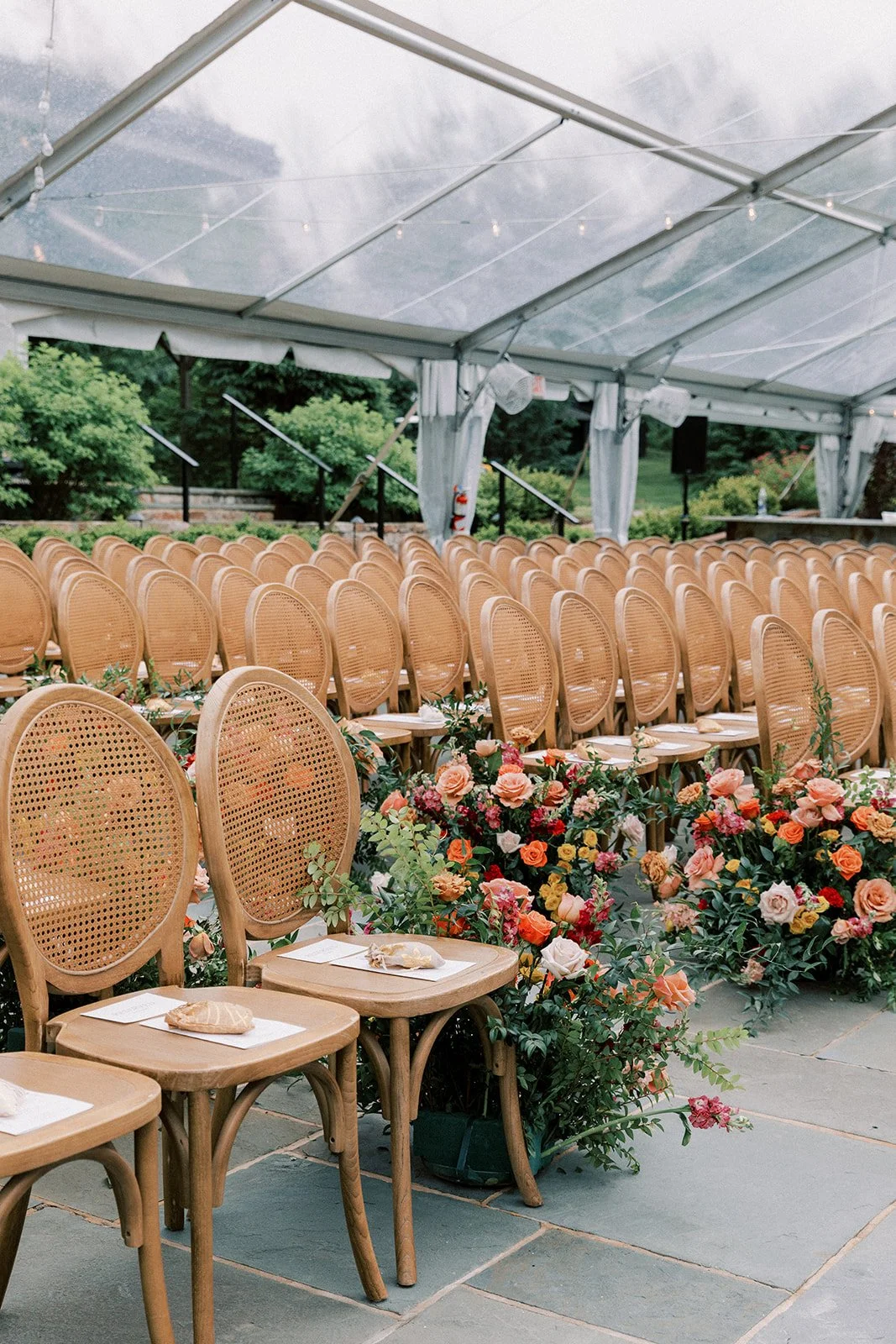 Empty chairs with floral arrangements and place settings inside a wedding tent.