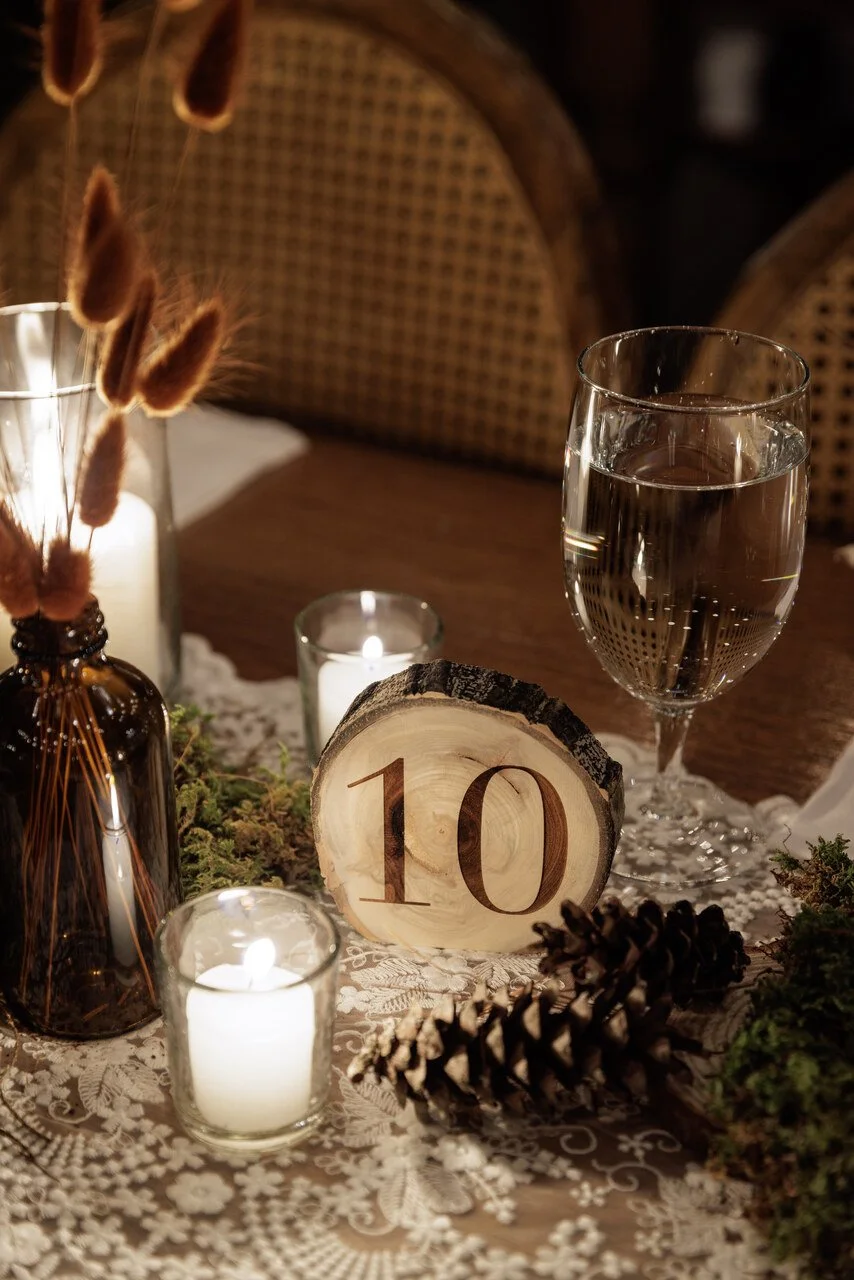 A table decorated with candles, pinecones, a wooden table number 10, a glass of water, and dried flowers, creating a cozy ambiance.