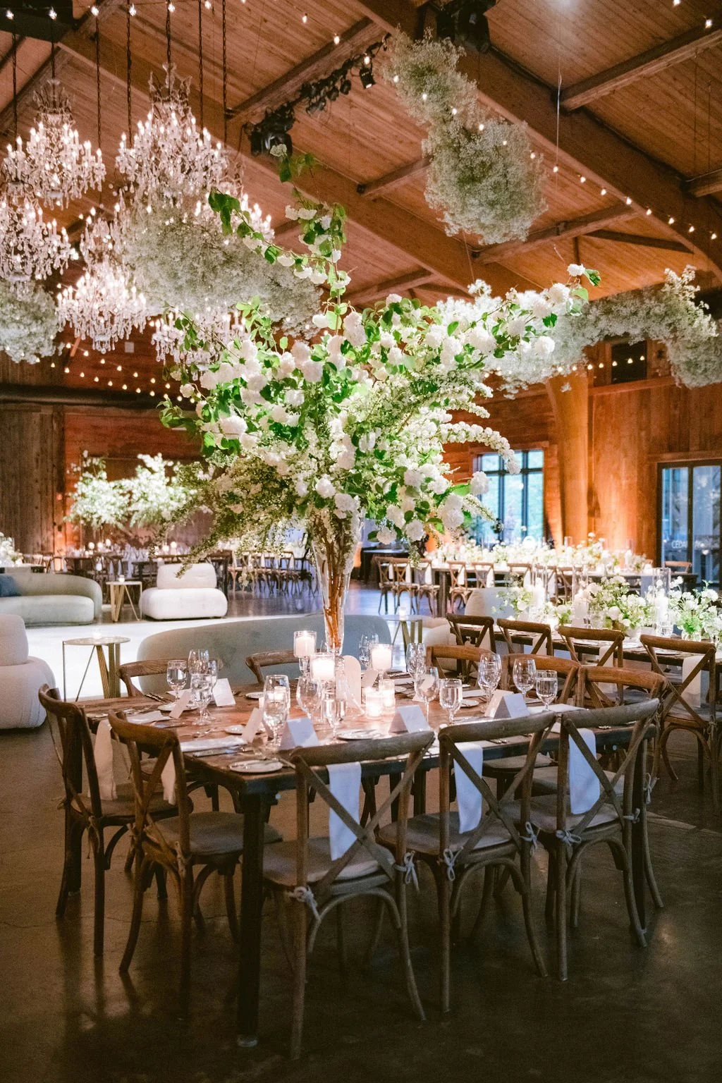 Elegant indoor wedding reception with a large floral centerpiece, white candles, and a warmly lit rustic wooden ceiling and walls.