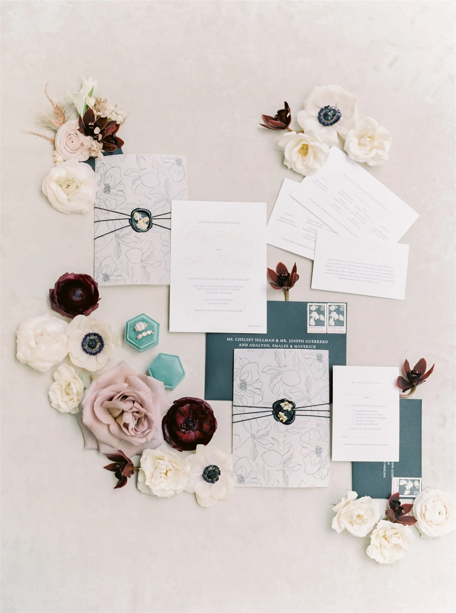 Flat lay of wedding invitations, floral arrangements, and decorative items including envelopes, floral cards, and jewelry on a white surface.