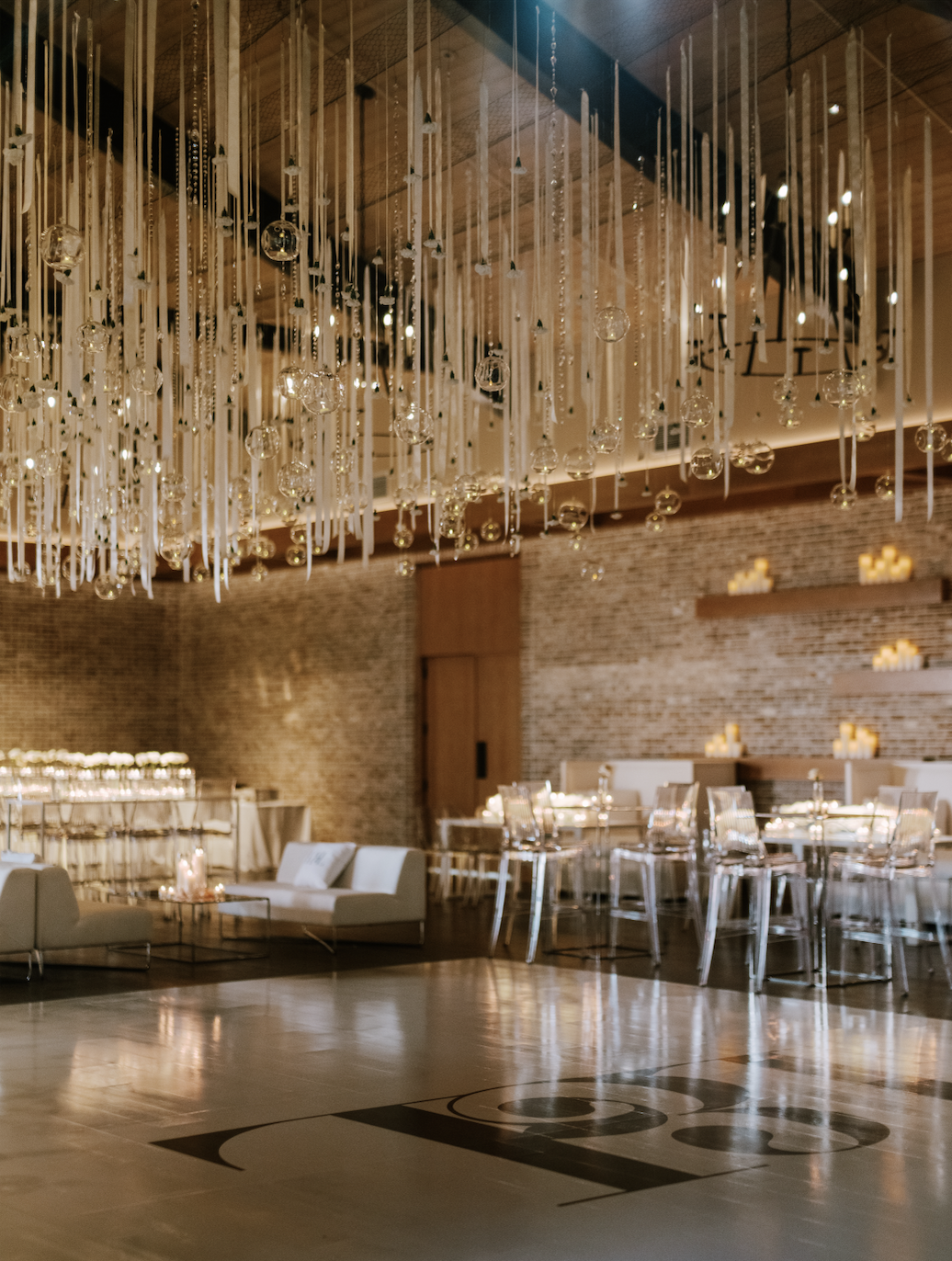 Elegant event space with a large chandelier hanging from a wooden ceiling, modern tables and chairs, and wall candles.