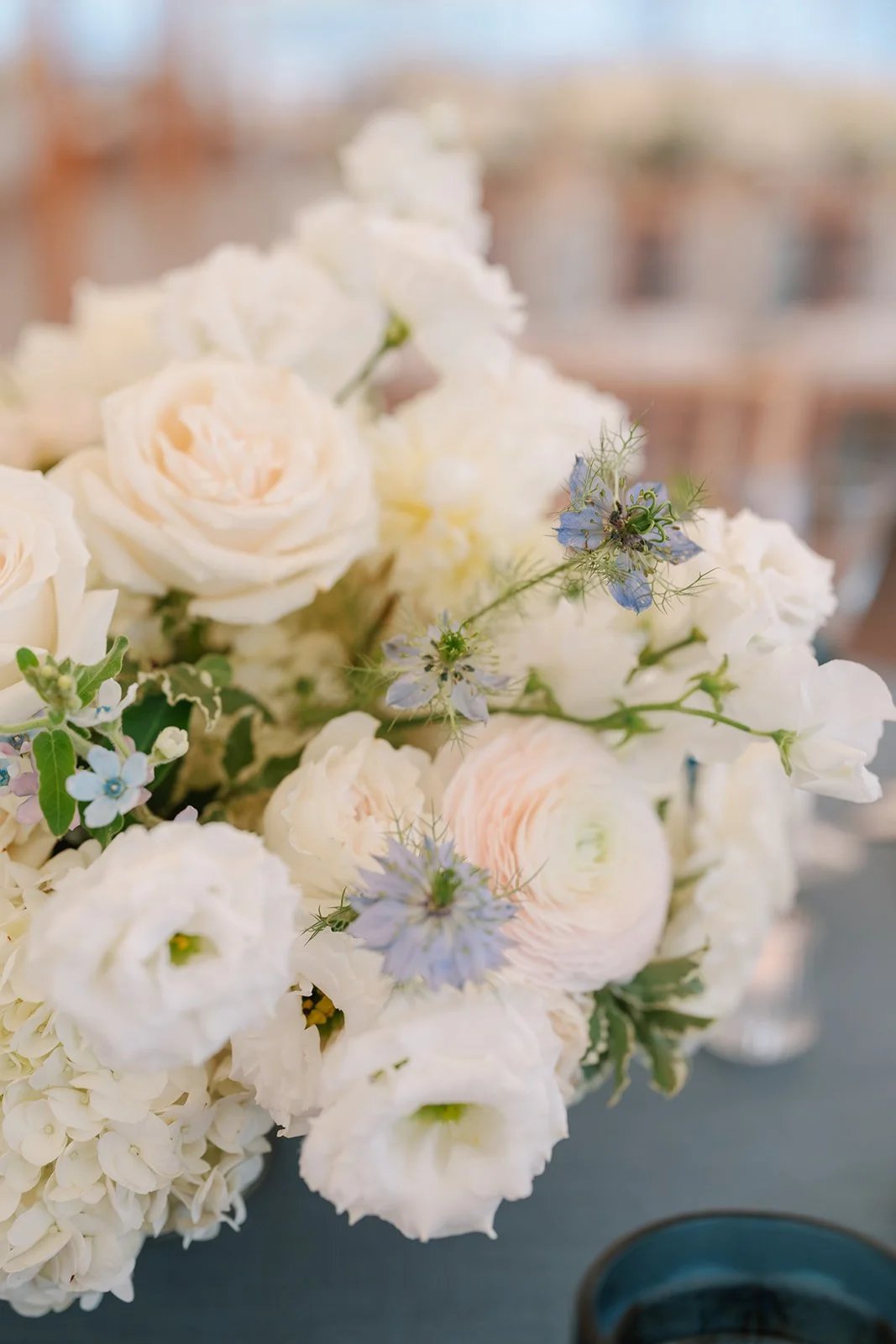 A bouquet of white and pale pink flowers with small blue blossoms and green leaves on a dark surface.