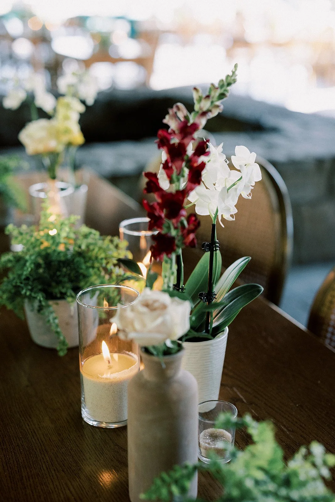 Decorative table setting with candles, potted plants, and flowers in white vases, illuminated softly in a cozy indoor environment.