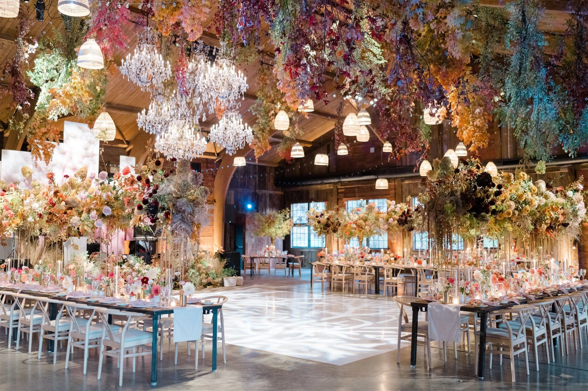 A decorated banquet hall with floral arrangements, chandeliers, and hanging lights, set for an event.
