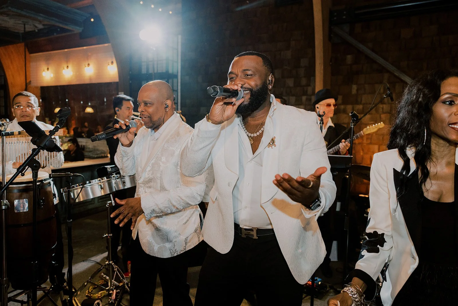 Group of singers performing on stage with musical instruments and microphones in a stylish indoor venue.