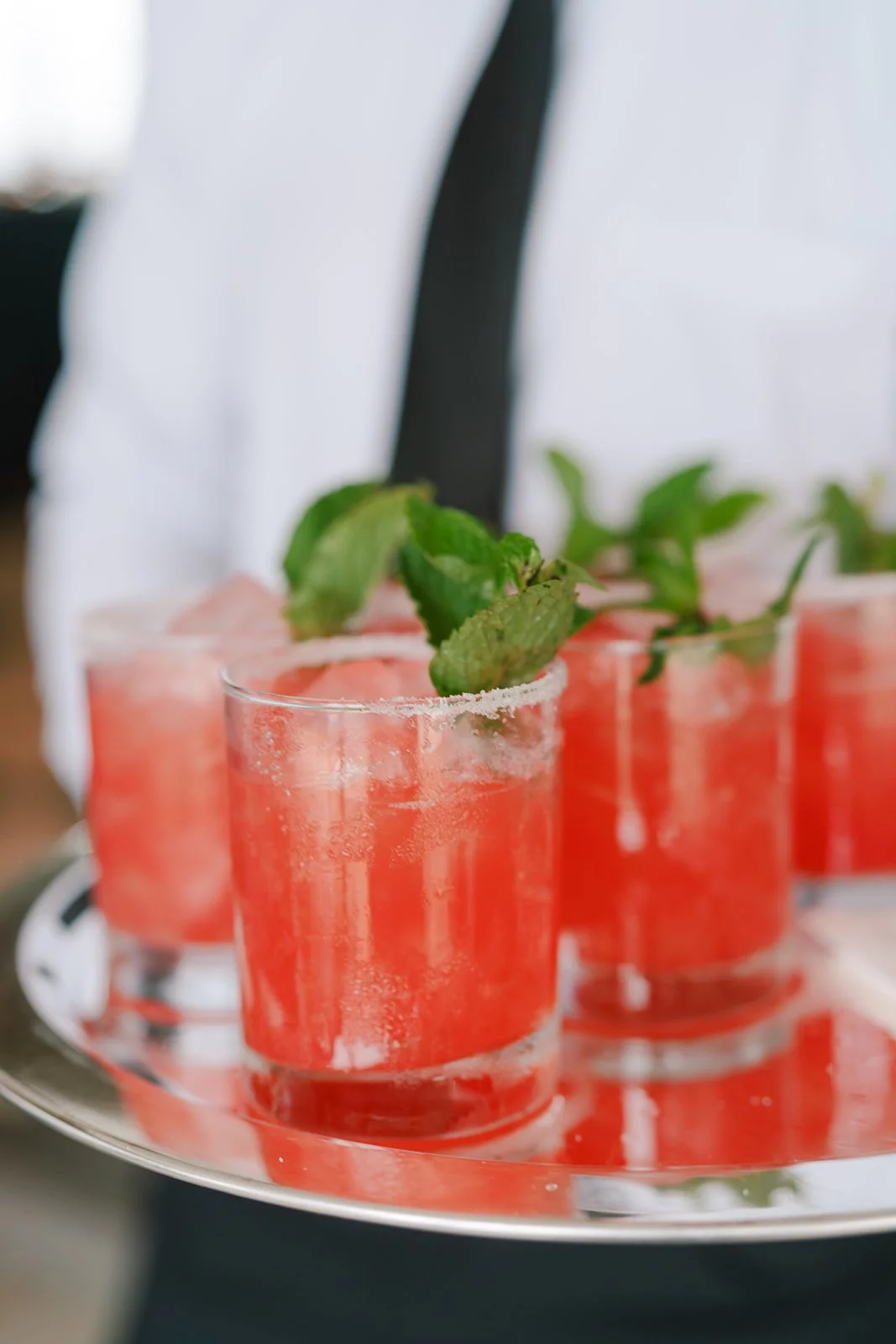 Three glasses of pink cocktail garnished with mint leaves on a silver tray.