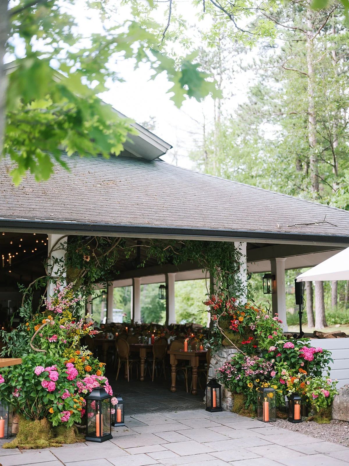 An outdoor event space decorated with pink, red, and yellow flowers, surrounded by lantern-style lights on the ground.