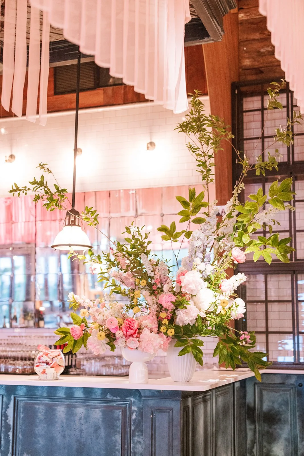 A display of pink and white flowers in white vases on a counter in a decorated indoor space.