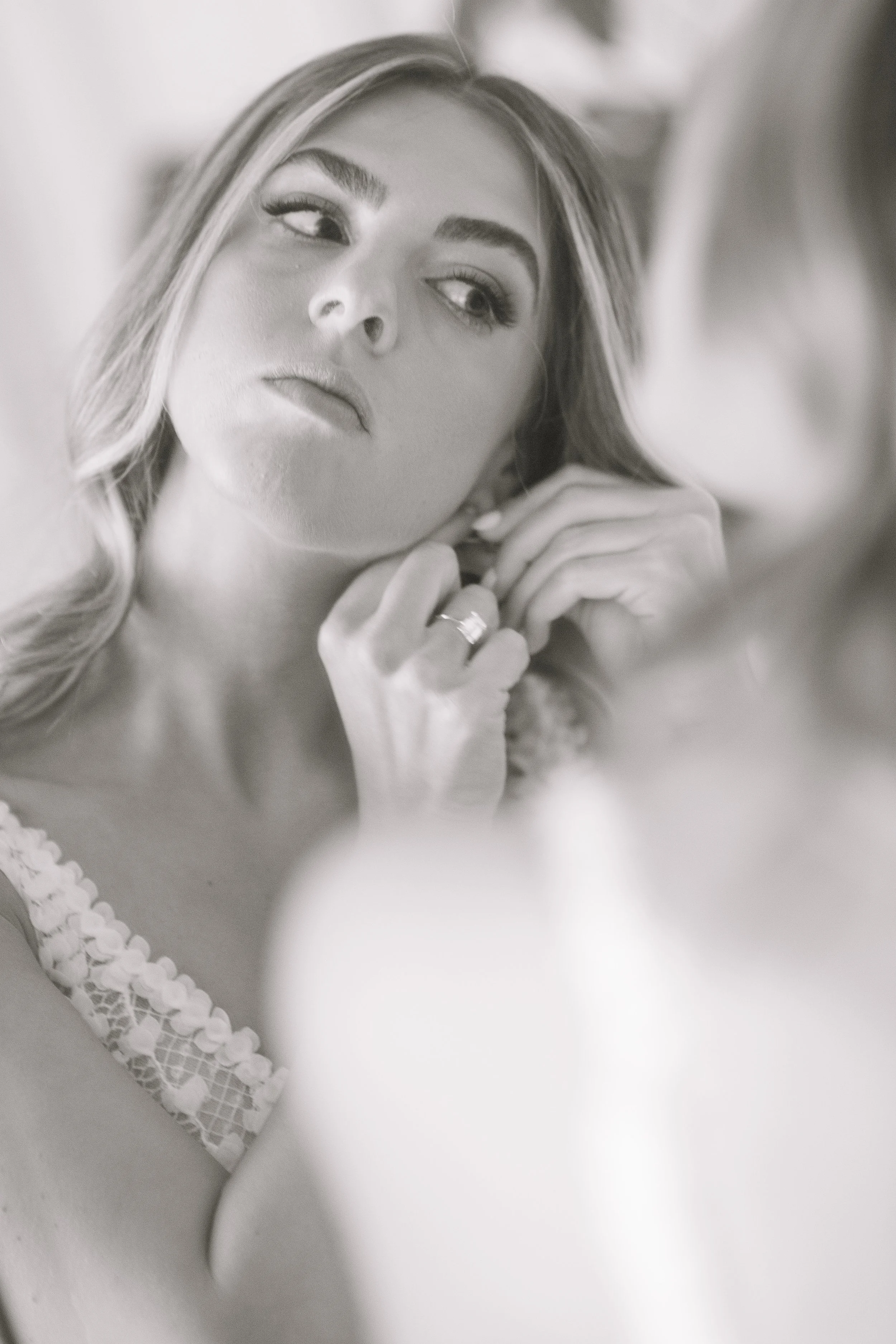 A woman looking at herself in a mirror, adjusting her earrings with a serious expression.