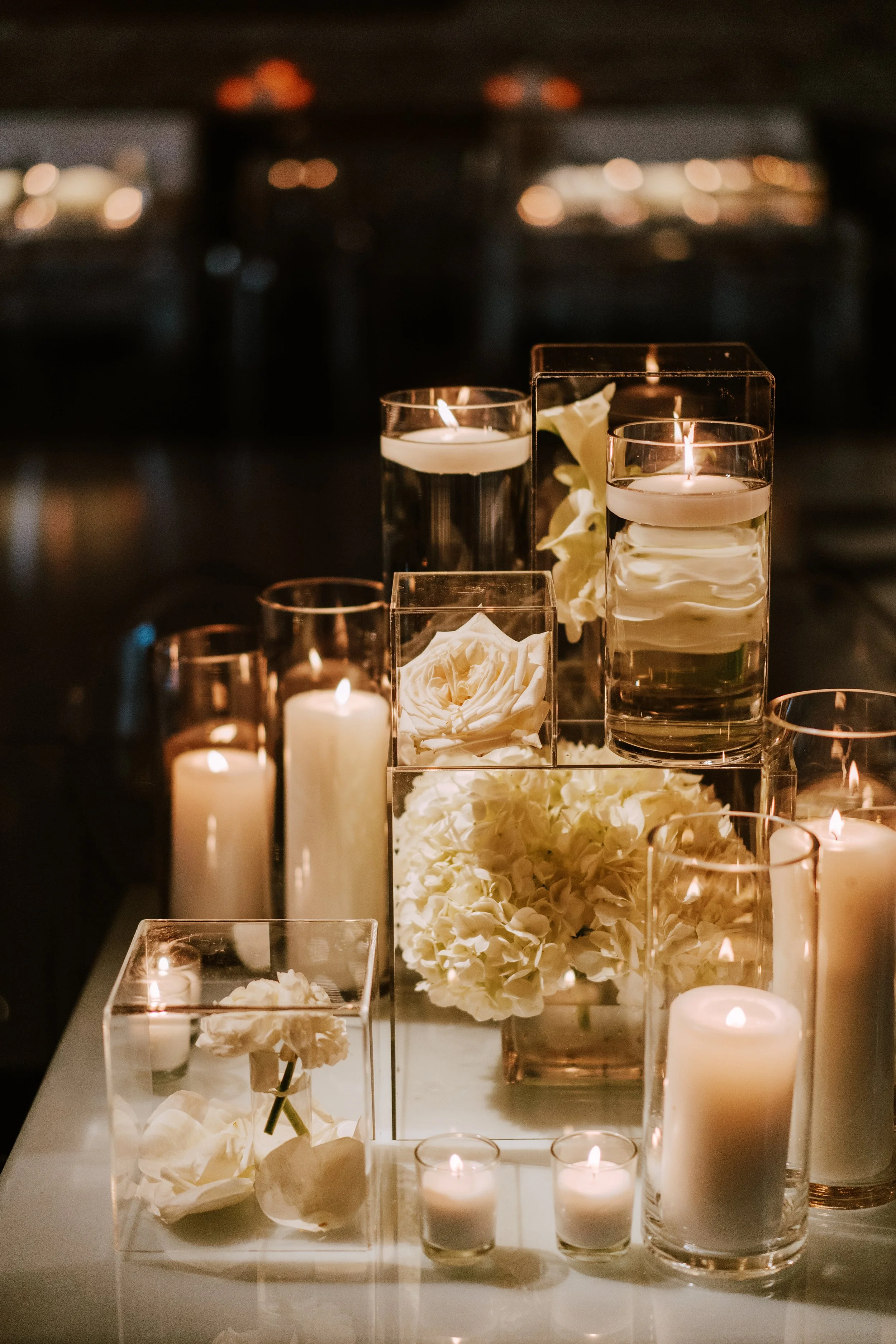 Arrangement of white flowers and floating candles in glass vases on a dark table, creating a romantic atmosphere.