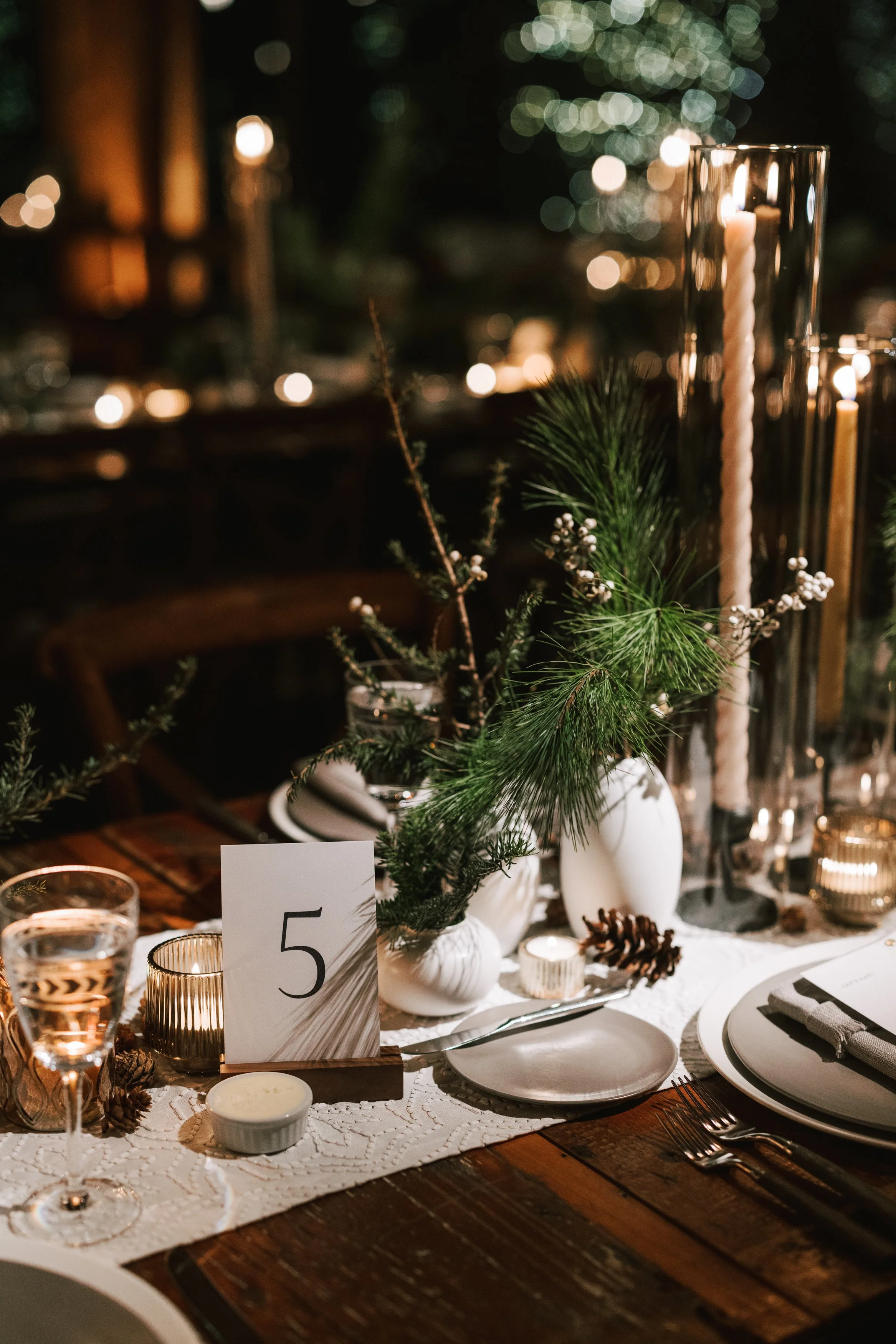 Elegant table setting with greenery, candles, pinecones, and table number five, set for a festive holiday dinner.