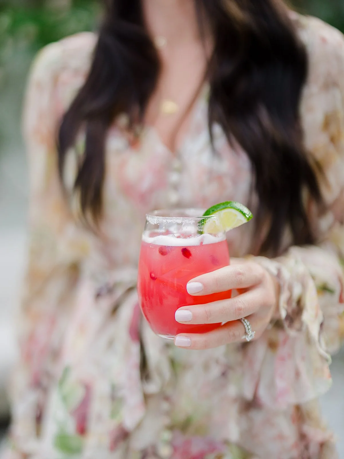A woman holding a glass of pink cocktail garnished with a lime wedge