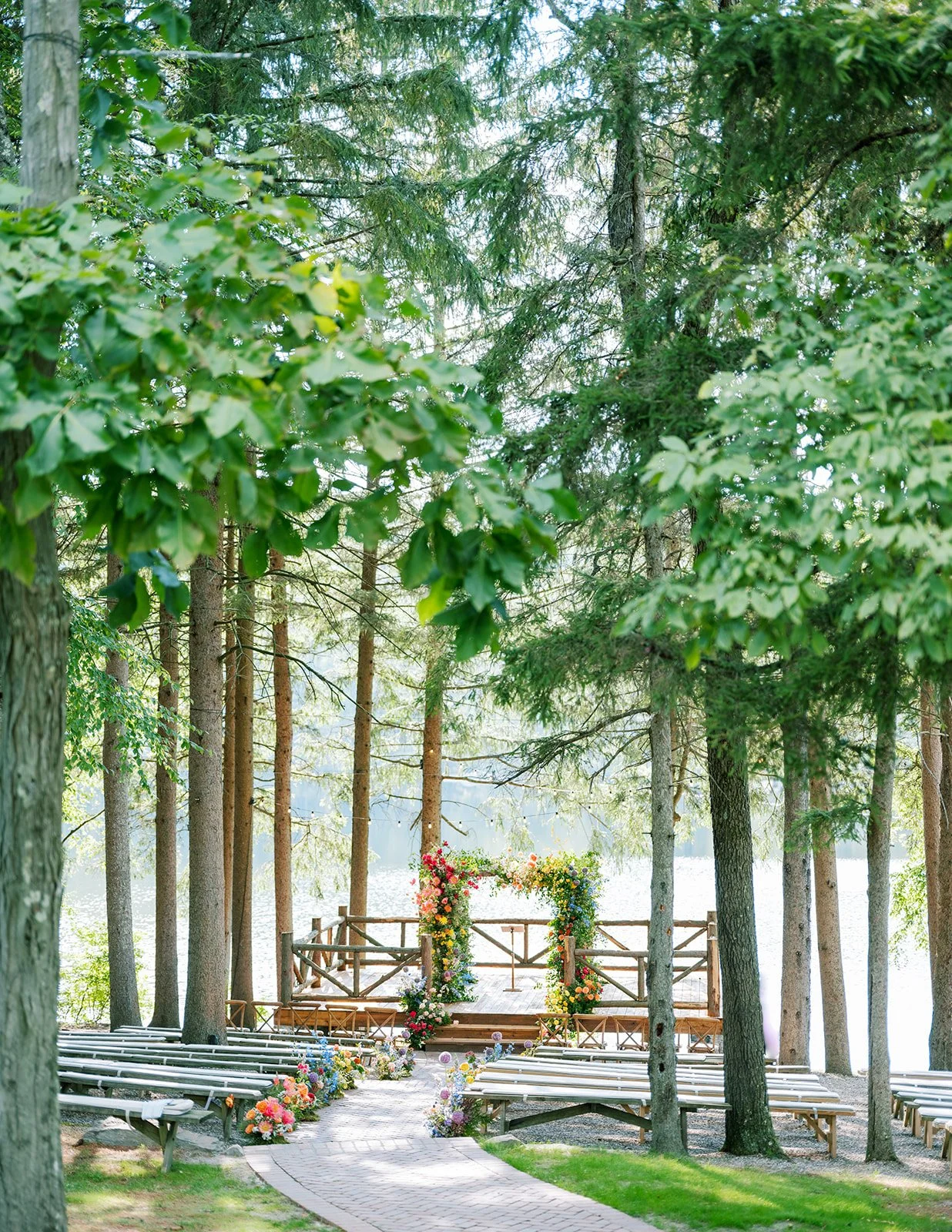 A wedding ceremony setup outdoors with a decorated archway, surrounded by benches and lush green trees by a lake.