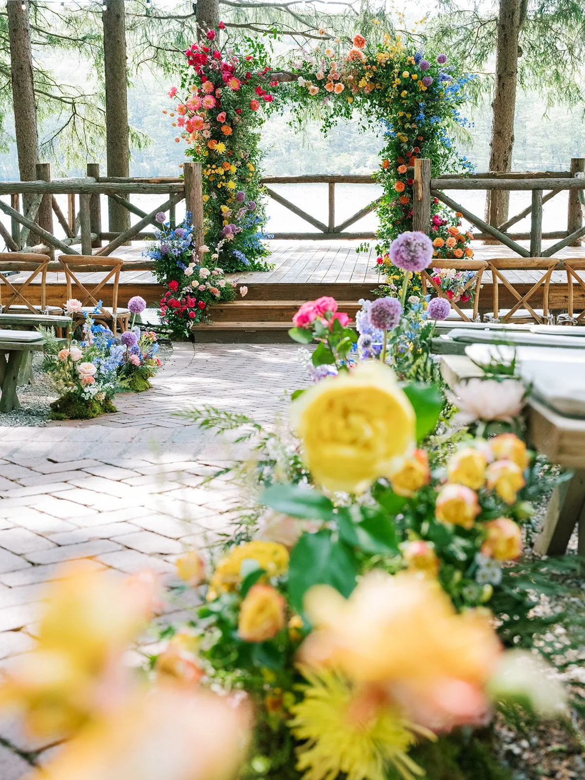 Colorful floral arch on wooden stage in outdoor setting with trees in background