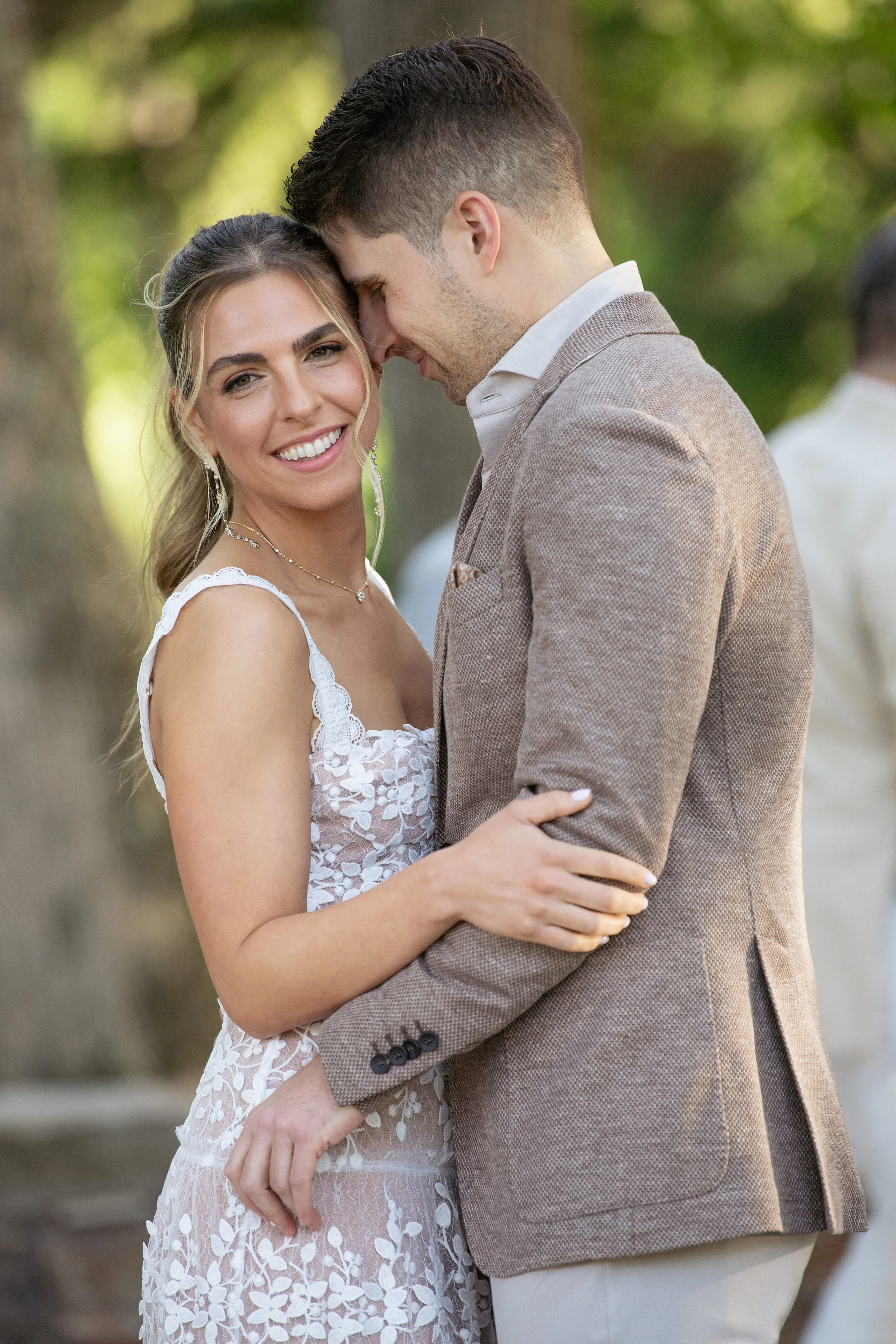 A smiling woman and a man with their foreheads touching, embracing outdoors during daytime.