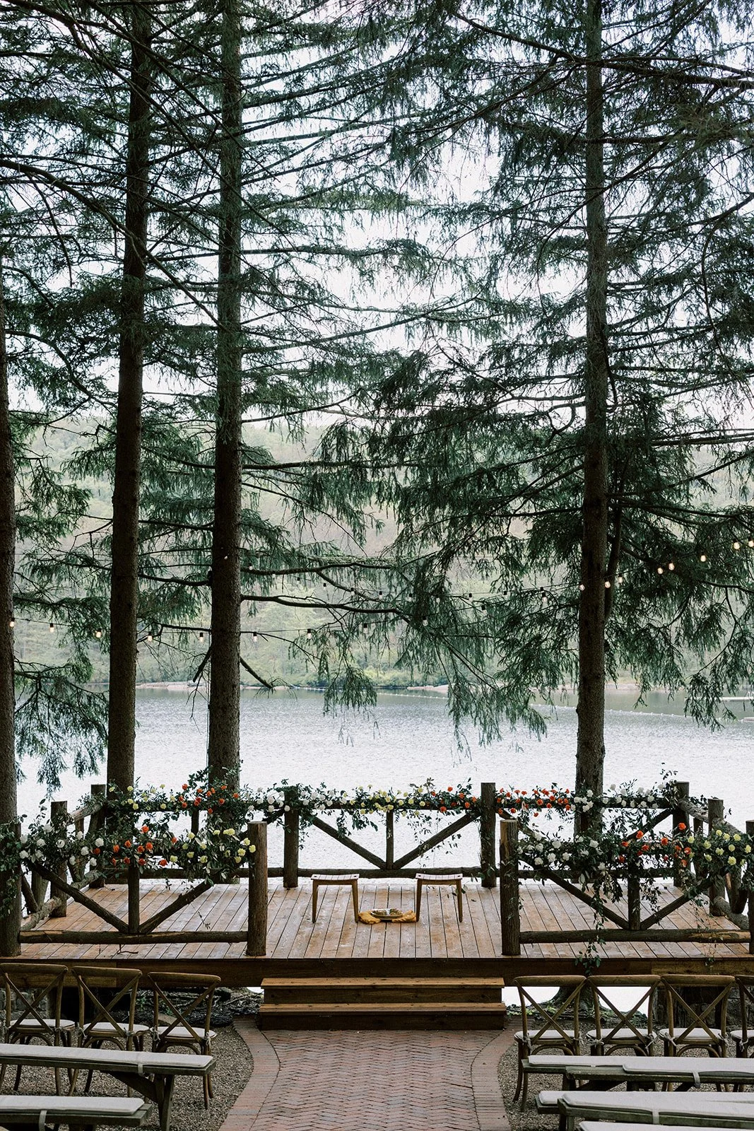 A decorated outdoor wooden stage with flowers, overlooking a lake surrounded by trees.