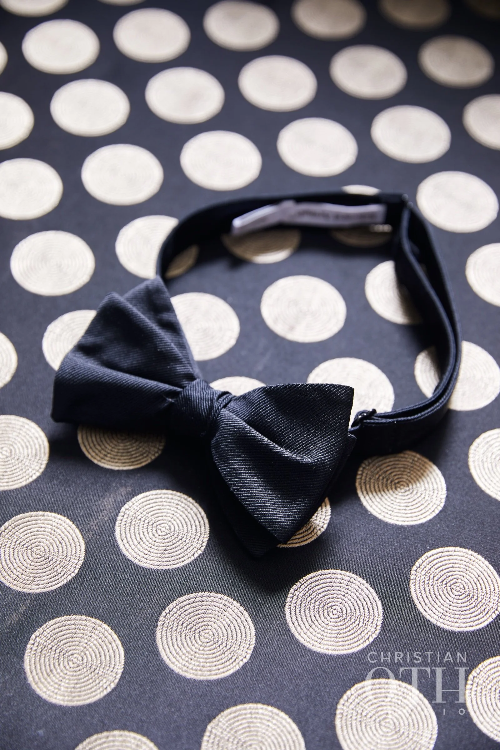 A black bow tie on a polka dot fabric background.